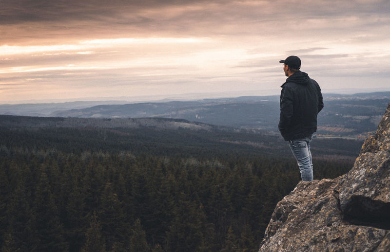 Rear view of man standing on cliff while looking at landscape