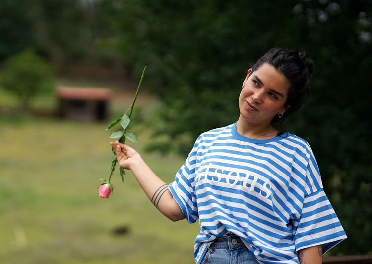Young woman smiling with a rose in the garden.
