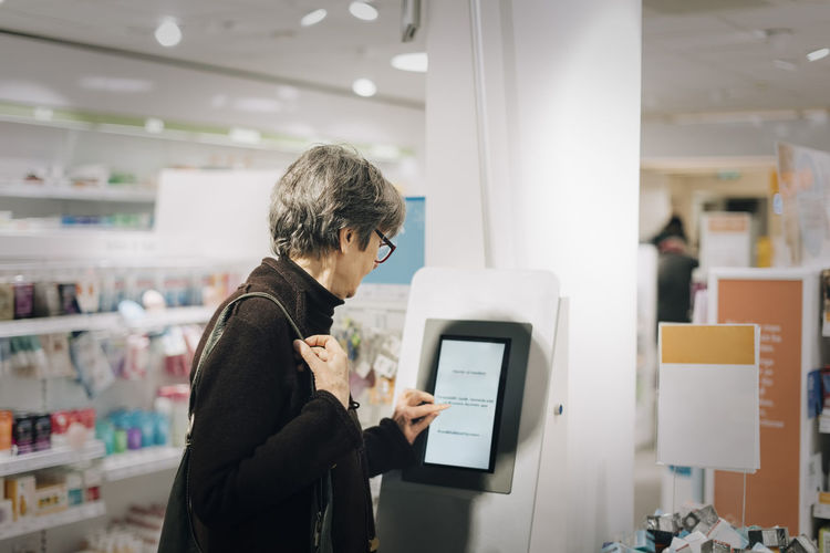 Side view of senior woman using kiosk at pharmacy store