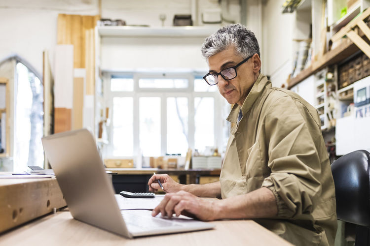 Mature male craftsperson working on laptop at workbench
