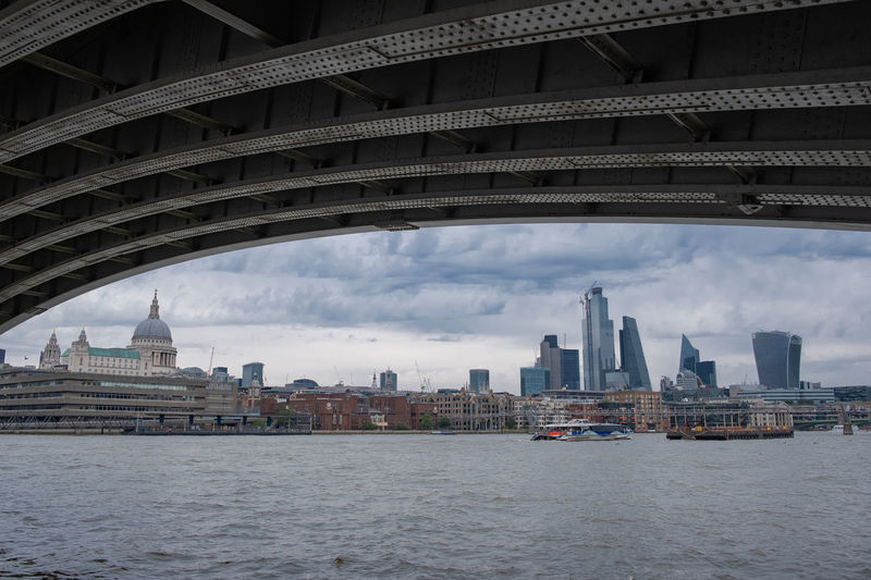 Bridge over river by buildings in city against sky