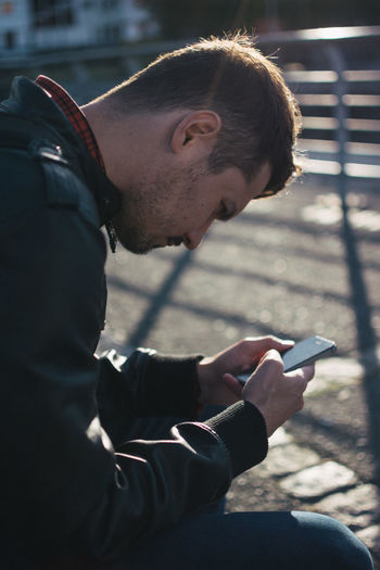 Serious young man using smart phone while sitting by street