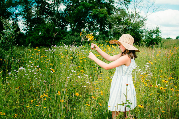 Teen girl holding a flower standing in wildflower field