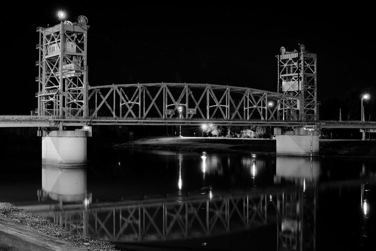 Bridge reflecting in river against sky at night
