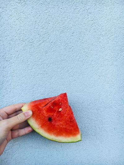 Cropped image of hand holding watermelon against wall