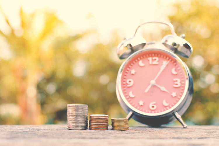 Close-up of coins stacked with alarm clock on retaining wall