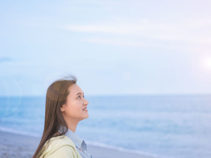 Portrait of young woman looking away at beach against sky