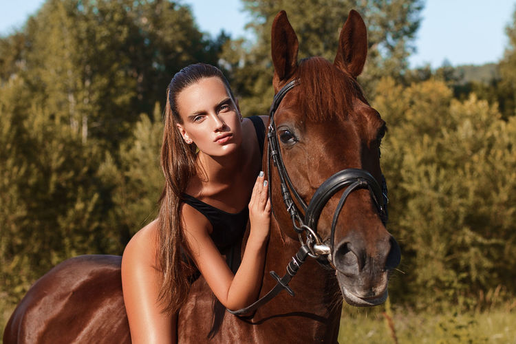 Portrait of seductive woman riding brown horse on field