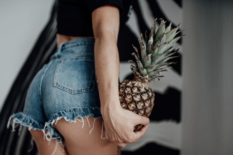 Midsection of woman wearing denim shorts holding pineapple
