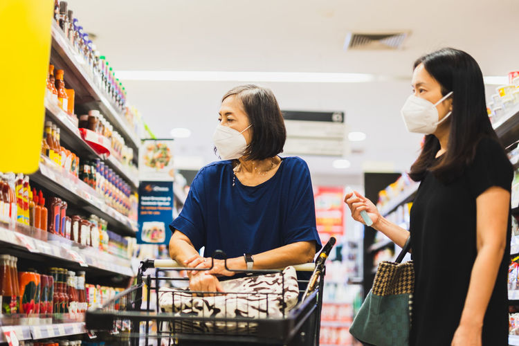 Senior woman and daughter in medical mask doing shopping in supermarket
