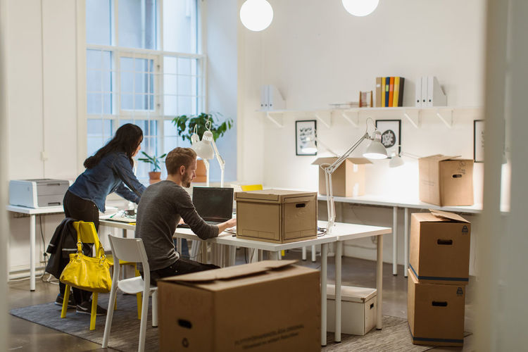 Business colleagues working at desk amidst cardboard boxes in illuminated creative office
