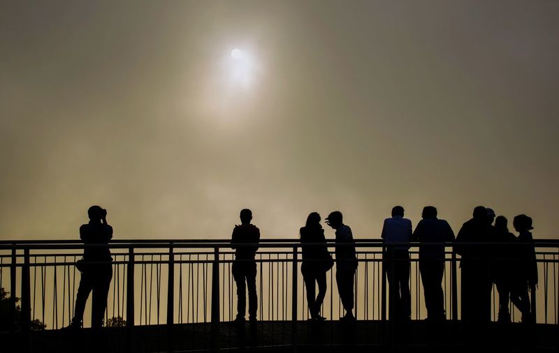 Silhouette people standing by railing against clear sky