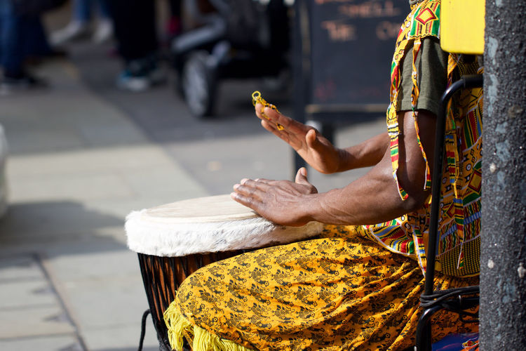 Midsection of woman playing bongo while sitting on chair at street