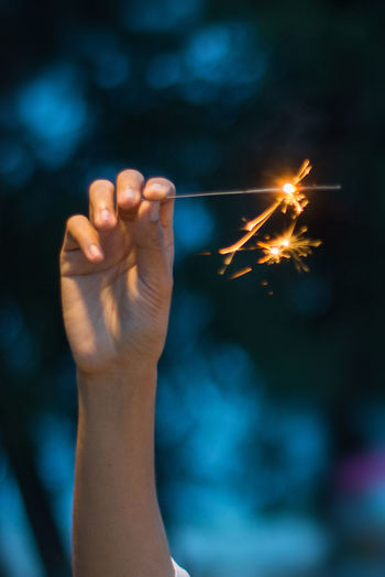 Cropped image of hand holding illuminated sparkler at dusk