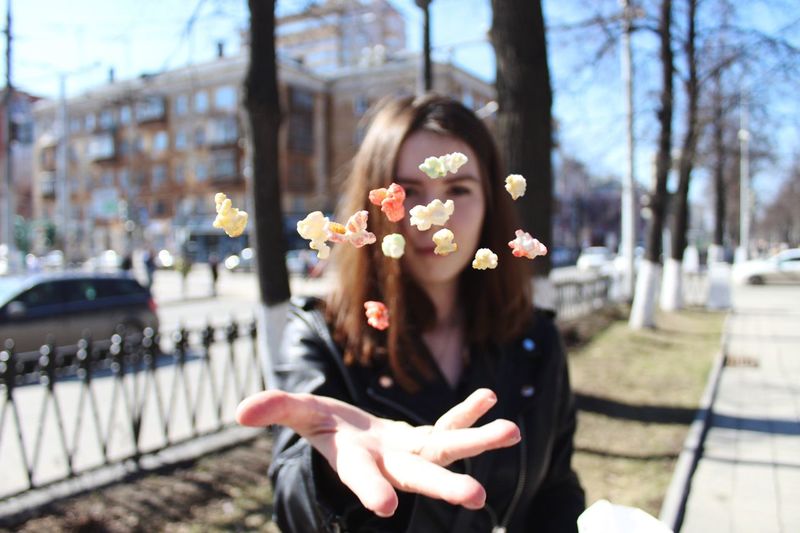 Portrait of woman throwing popcorn while standing in city