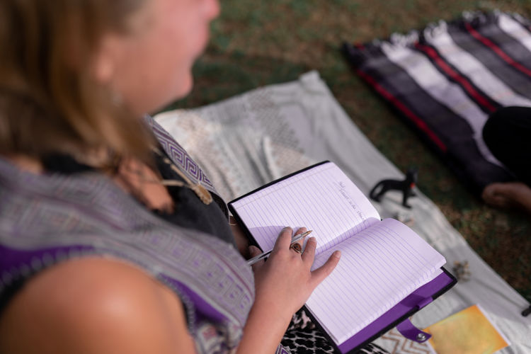 From above cropped unrecognizable female shaman taking notes in planner during meditation session in nature