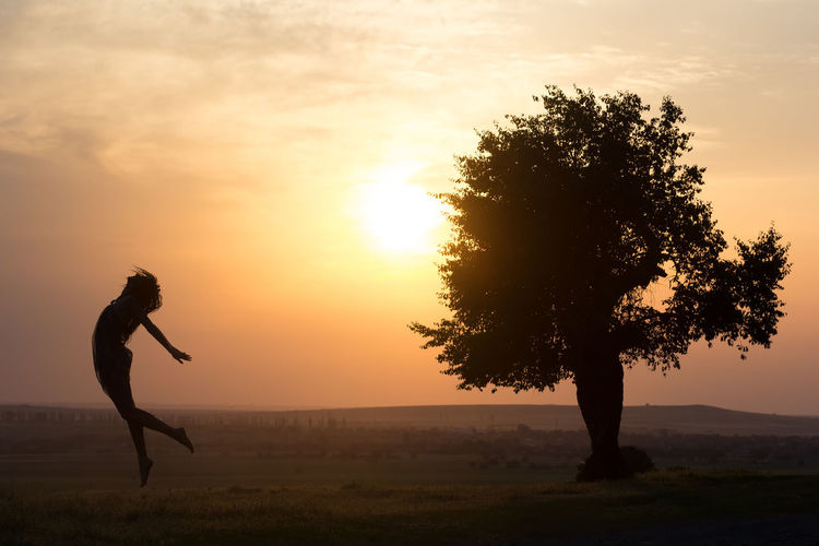 Silhouette woman jumping over field against sky during sunset
