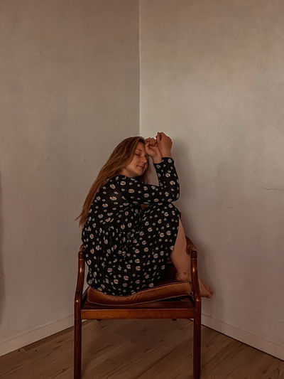 Woman sitting on chair against wall