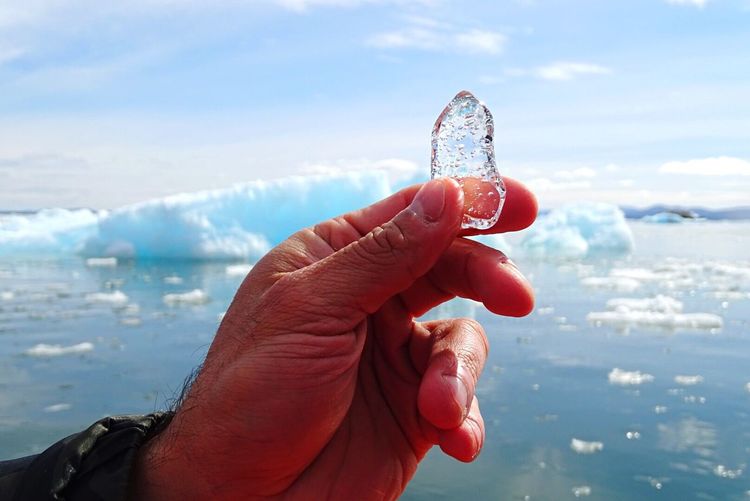 Cropped image of man holding ice crystal against glacier in sea
