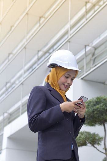 Low angle view of female architect using smart phone while standing against office building