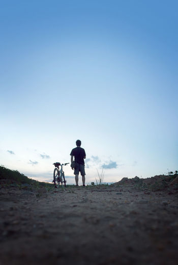 Rear view of man with bicycle on road against sky