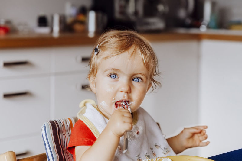 Portrait of cute baby girl eating food at home