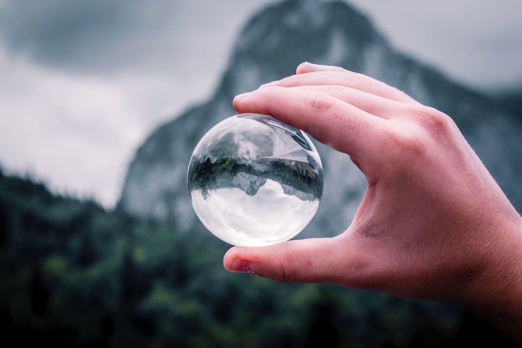 Cropped hand holding crystal ball against mountain