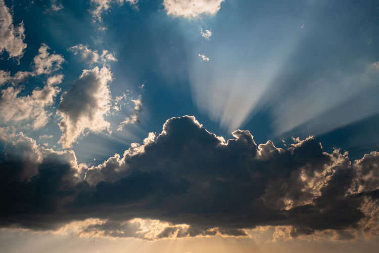Low angle view of sunlight streaming through clouds