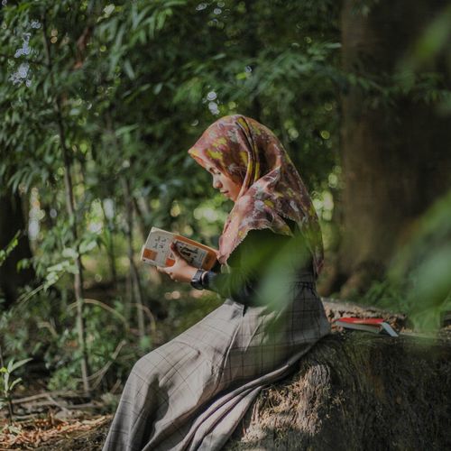 Side view of woman reading book in forest