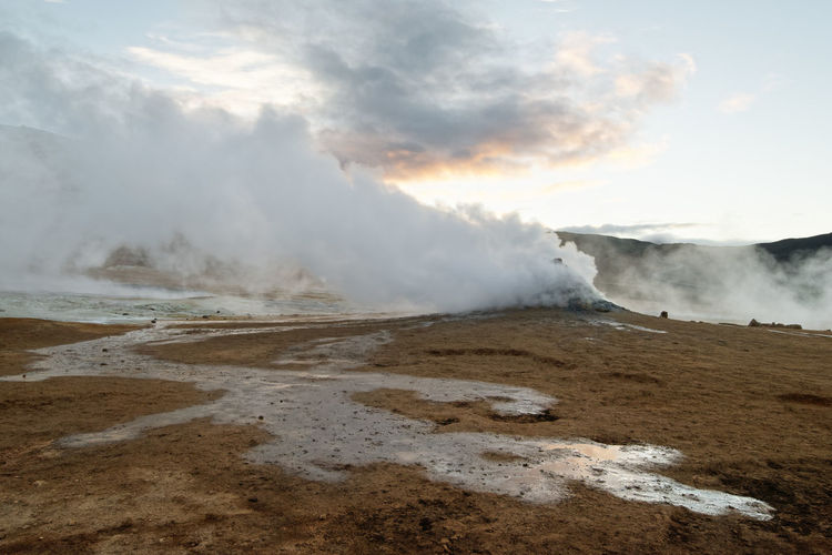 Wide volcanic landscape with a water surface and a lot of steam, which is blown sideways by the wind