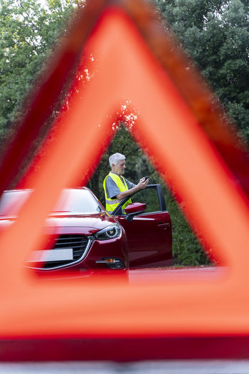 Close up of a warning triangle in front of a senior man's broken car on a country road