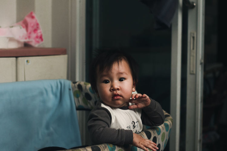Portrait of cute boy sitting on bed at home
