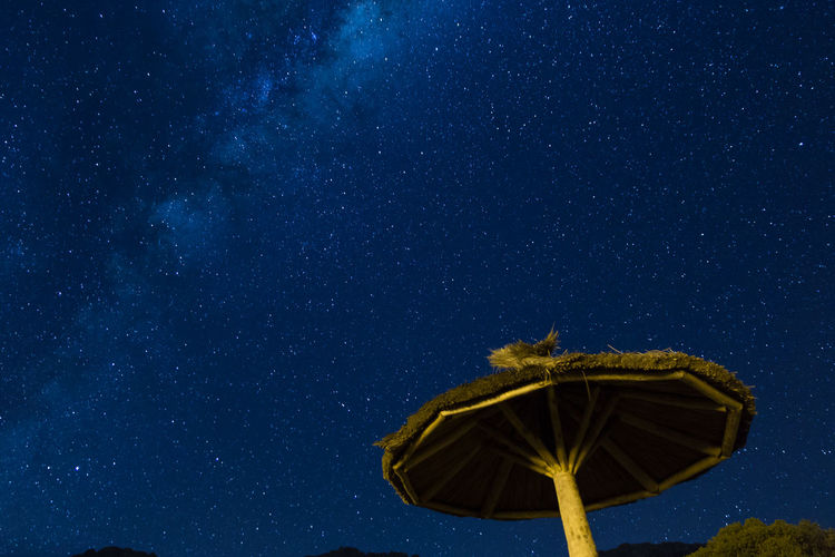 Low angle view of sunshade against star field in blue sky during night