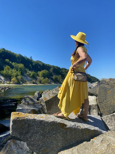 Side view of woman standing on rock against clear sky