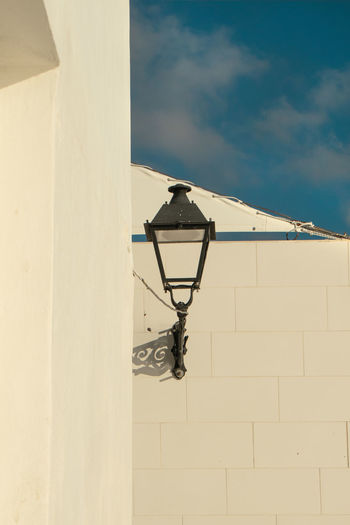 Low angle view of electric lamp on wall against sky