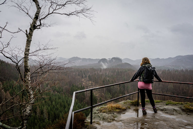 Rear view of woman walking on mountain against sky in fog and rain