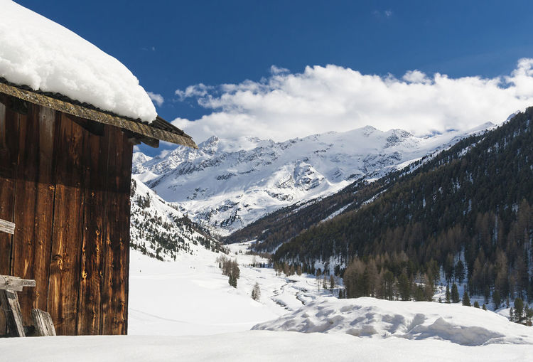 Log cabin on snowcapped mountain against sky