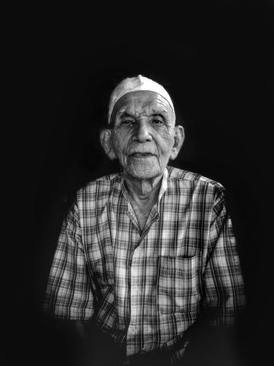 Portrait of senior man in skull cap sitting against black background
