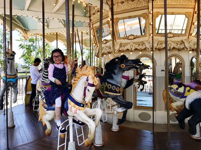 Portrait of girl sitting on carousel horses at amusement park