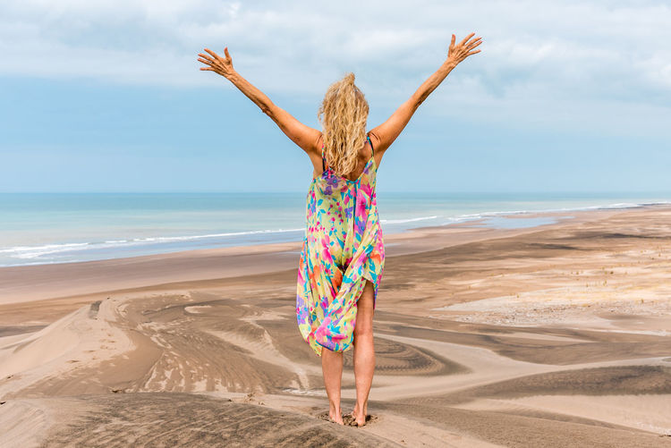 Back of an adult blonde woman standing on the desert gesturing freedom with the arms raise