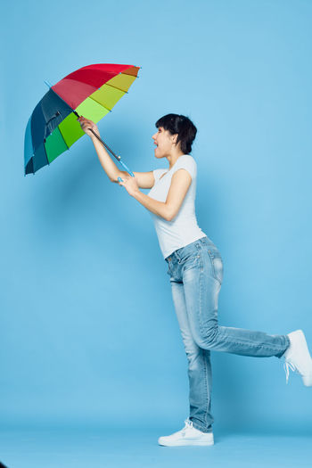 Woman with umbrella standing against blue background
