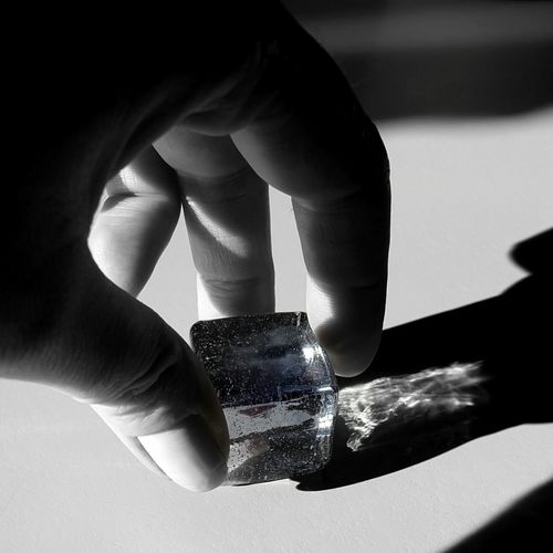 Cropped image of person holding cube shape crystal on table