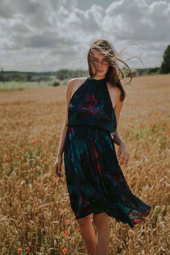 Young woman standing on field against sky