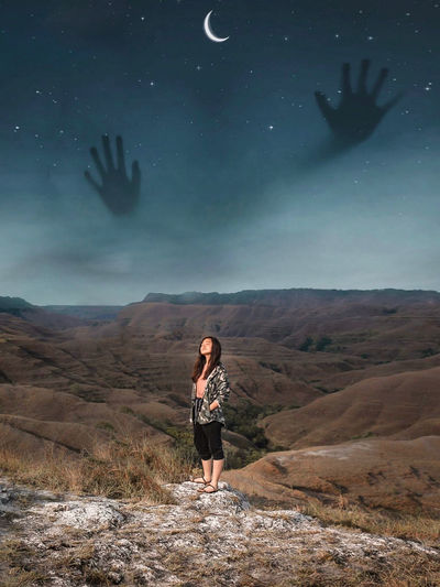 Digital composite image of teenage girl standing on mountain at night