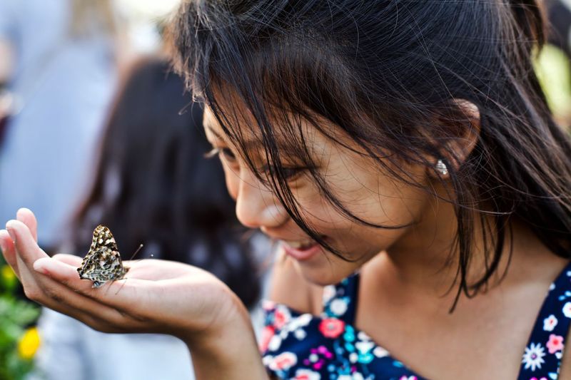 Close-up of cute smiling girl looking at butterfly on hand