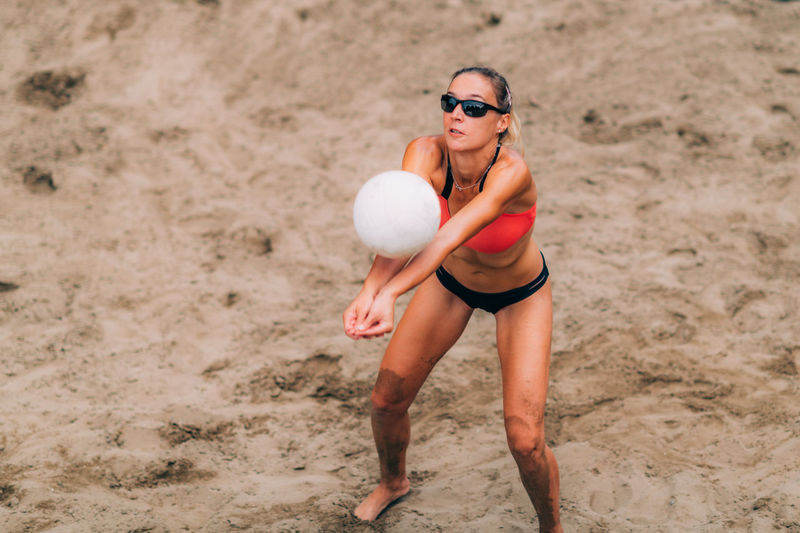 Low section of woman playing with ball on sand at beach