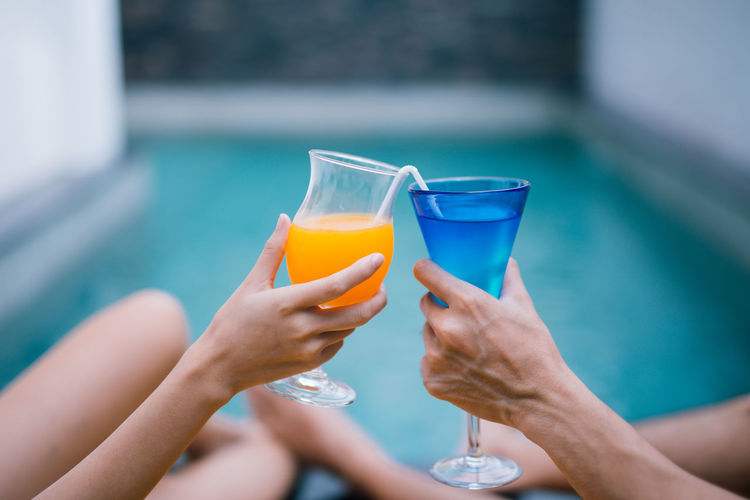 Midsection of friends toasting drinks at poolside