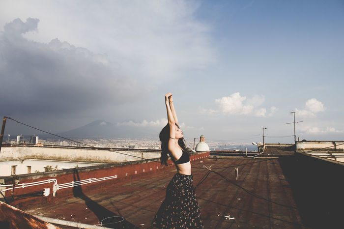 Woman exercising on roof against sky