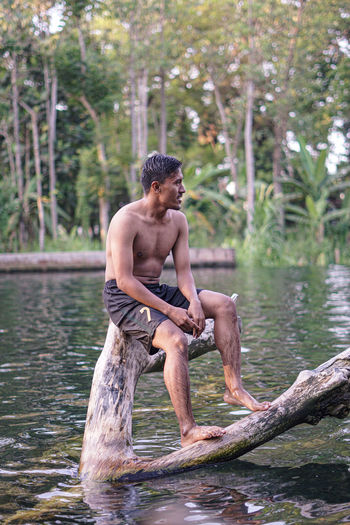 Young man sitting in lake against trees