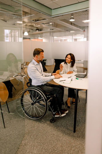 Smiling businesswoman discussing sales plans with disabled manager while sitting in board room